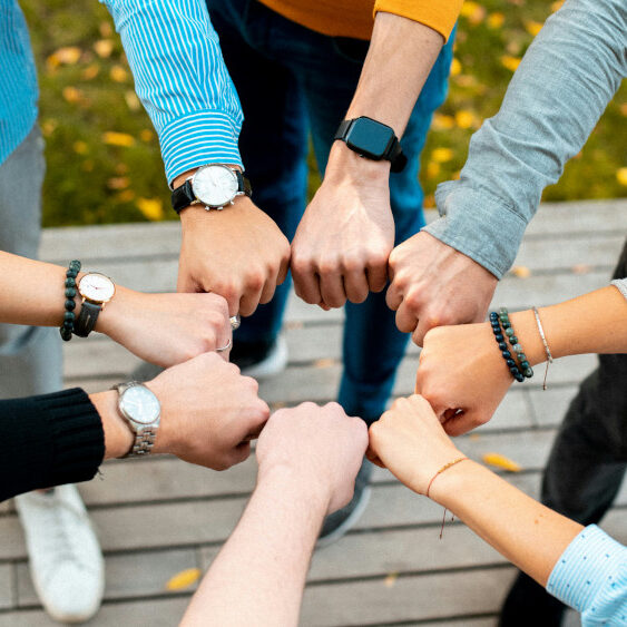 Mehrere Menschen stoßen ihre Fäuste in der Mitte zusammen und symbolisieren Gemeinschaft und Zusammenhalt.